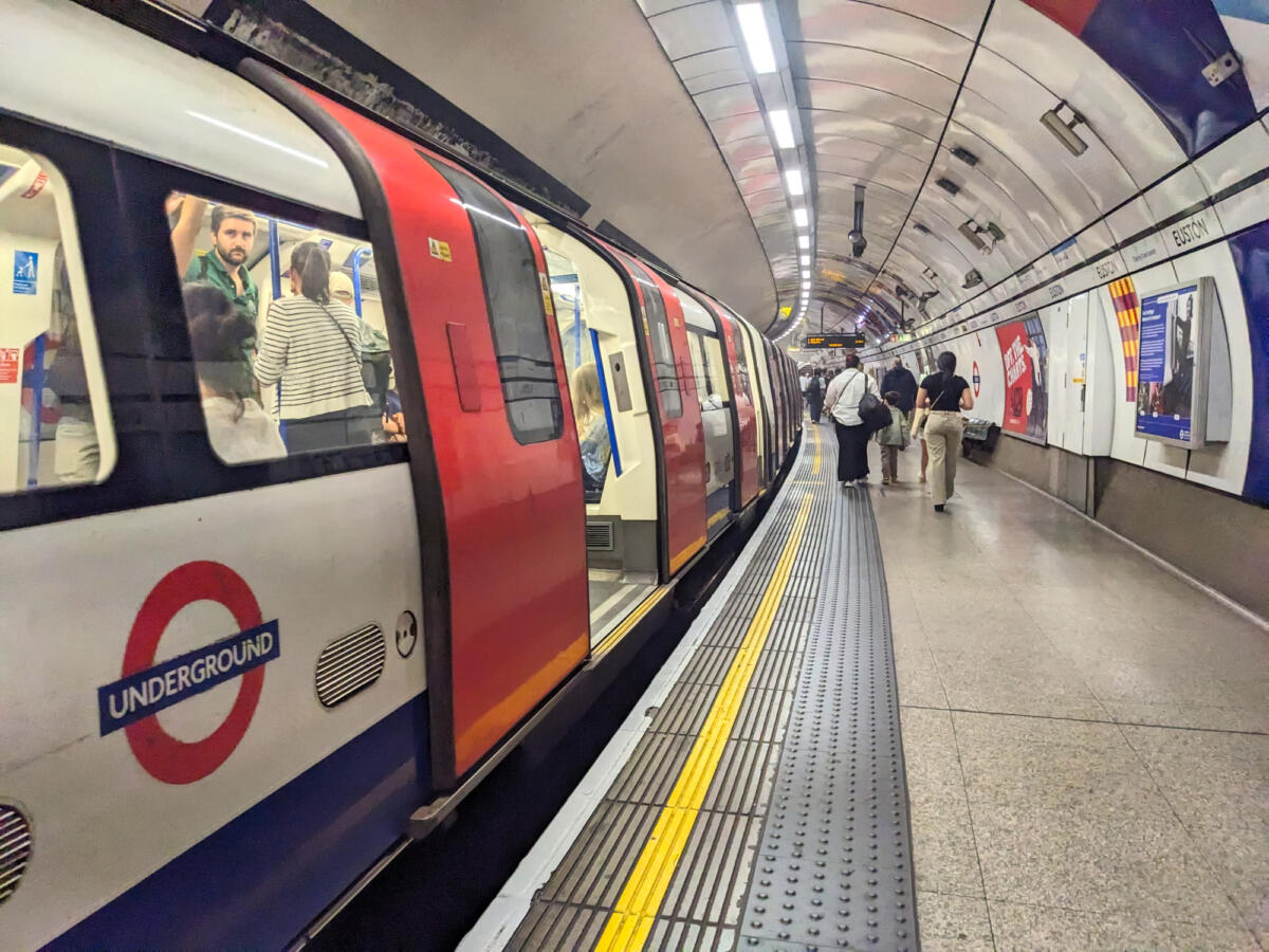 A classic red and white Northern Line London Underground train stopped with open doors at the curved platform of Euston station as passengers leaving the train