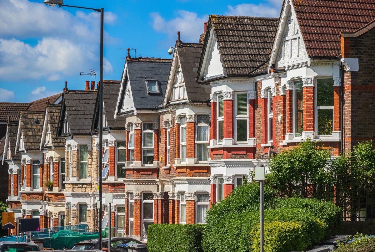 Row of traditional red-brick terraced houses on a residential street beneath a bright blue sky.