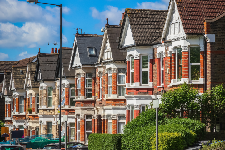 Row of traditional red-brick terraced houses on a residential street beneath a bright blue sky.