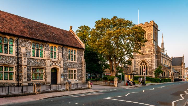 Historic stone church and neighbouring building beside a tree-lined street with a bus stop.
