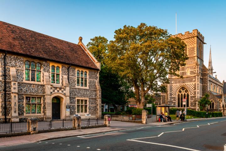 Historic stone church and neighbouring building beside a tree-lined street with a bus stop.